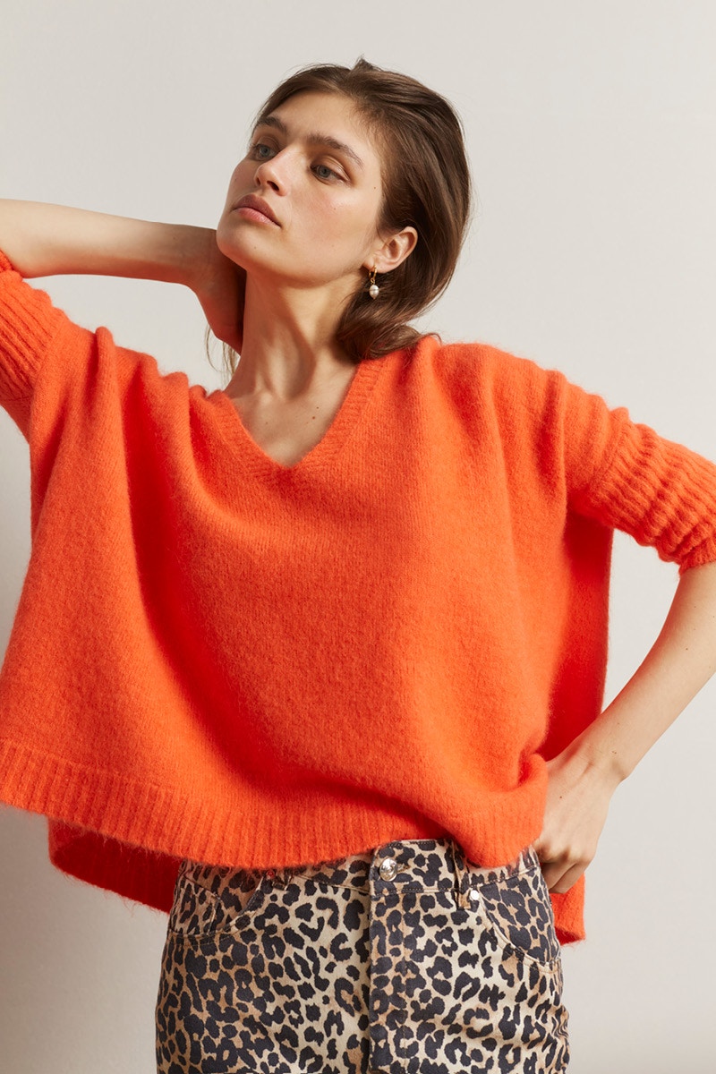 Frau mit einem orang-rotem Pullover und einer Hose im Leodruck.