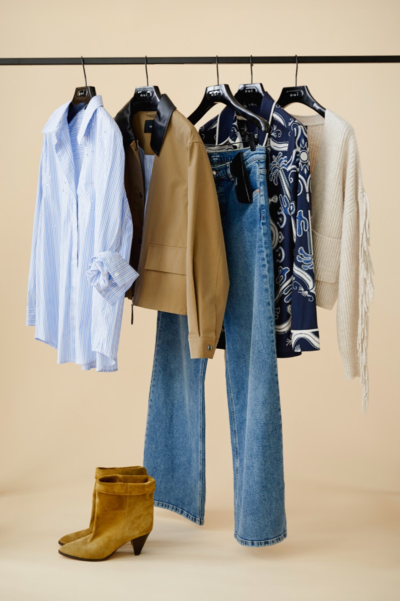 Kleidung an einer Stange. Vorne eine blau weiss gestreifte Bluse, dann eine braune Jacke, dahinter eine Jeanshose, eine dunkelblaue Bluse mit weissem Aufdruck und ganz hinten eine beige Strickjacke.