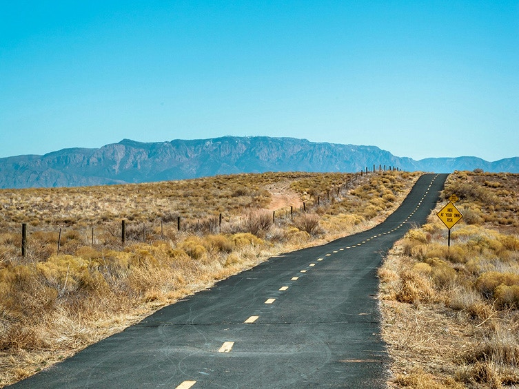 Eine gerade lange Straße durch eine wüsten Landschaft.