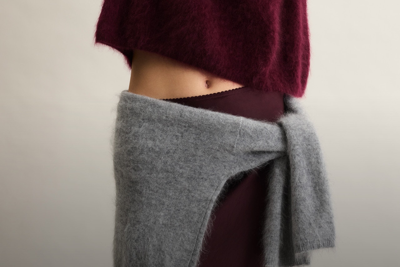 Bild von einer Körpermitte, man sieht oben einen brugundfarbenen Pullover, etwas Haut und Bauch, dann einen burgundfarbenen Rock und um die Hüften gebunden einen grauen Cardigan.