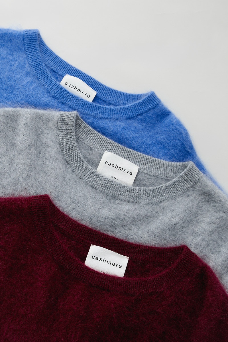 Bild mit drei gelegten Pullovern von denen der Halsausschnitt zu sehen ist. Die Pullover sind blau, grau und burgund rot.