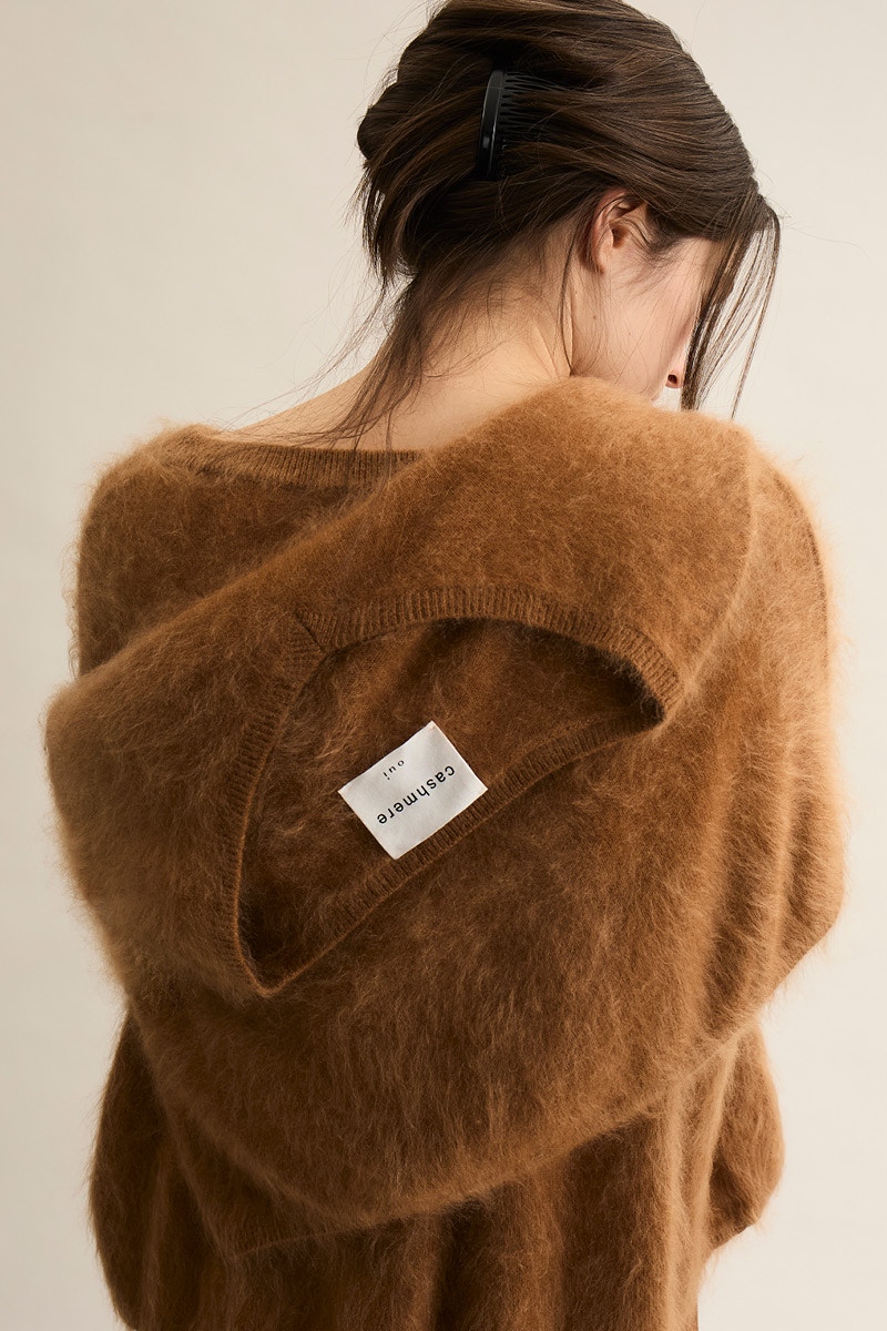 A woman from behind, wearing a brown jumper and another brown jumper around her shoulders.