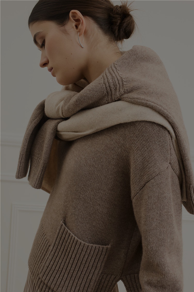 Frau trägt einen braunen Pullover und um die Schultern zwei weiter Pullover einen in grau und einen in beige.