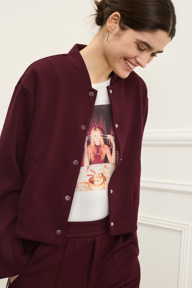 Frau trägt eine burgundrote Jacke mit passender Hose und darunter ein weisses T-Shirt mit Druckmotiv.