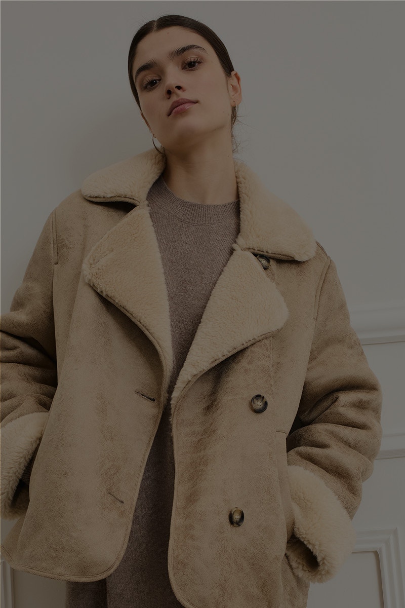 Woman wears a beige jacket with a brown jumper underneath.