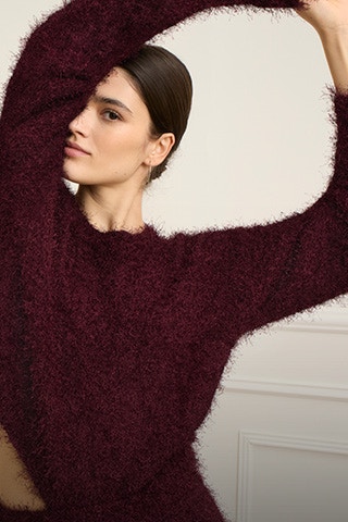 Frau mit Armen nach oben trägt einen burgundfarbenen flauschigen Pullover. 