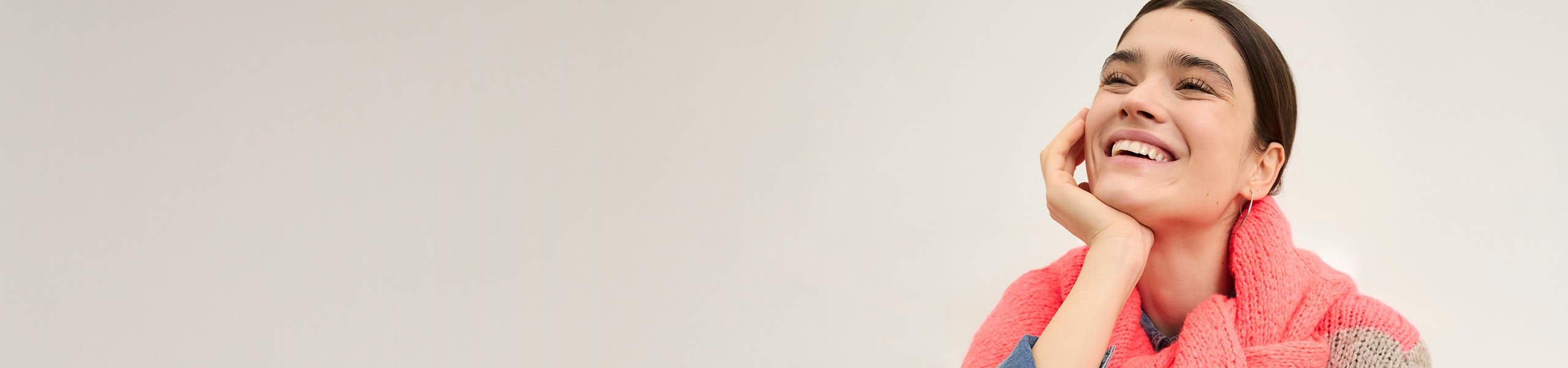 Smiling woman wears a grey and pink striped jumper with a pink jumper over her shoulders.