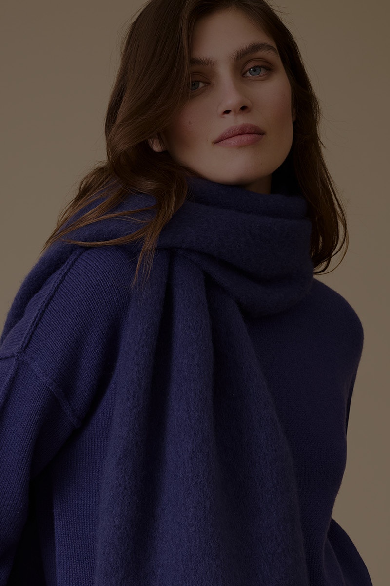 Frau trägt einen blauen Pullover und einen langen blauen Schal um ihren Hals.