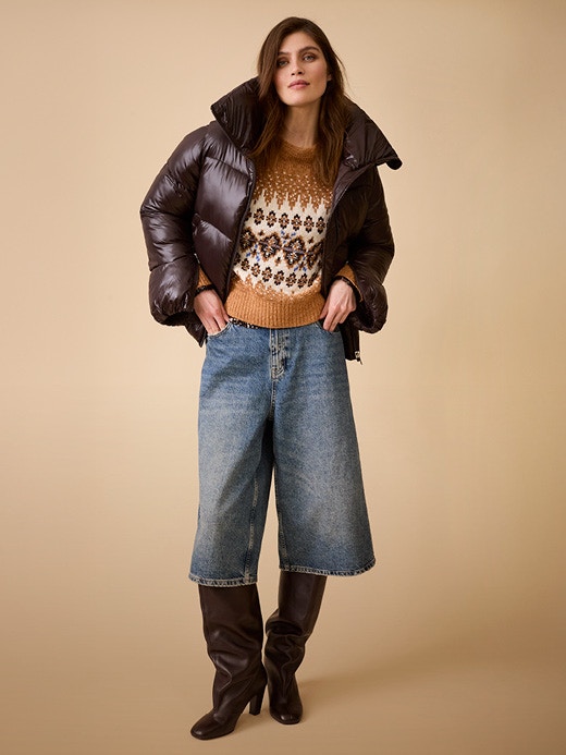 On the right is a woman wearing a brown puffer jacket with a brown jumper underneath, patterned with dark brown, white and beige, and jeans shorts.