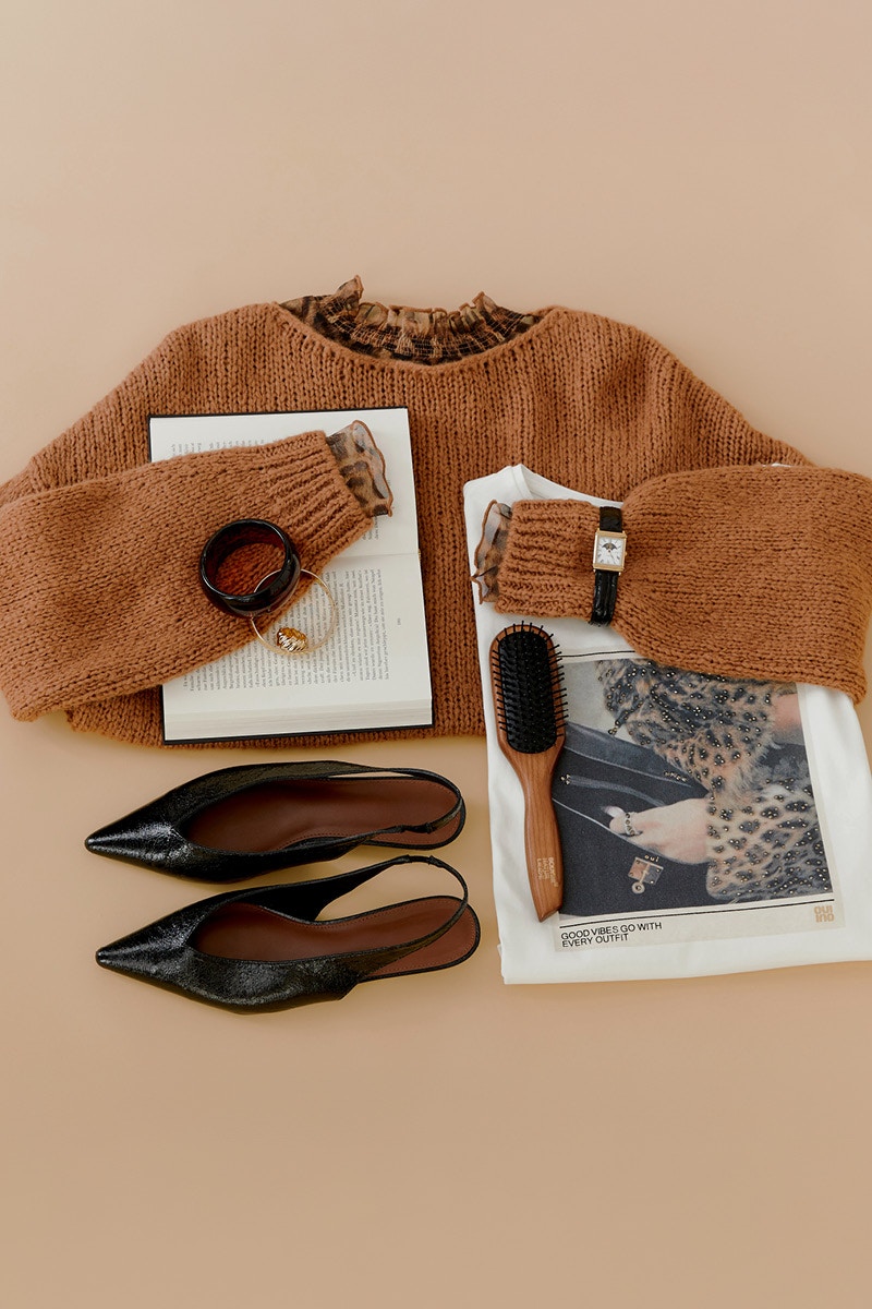 A brown jumper lies folded on the floor and a leo blouse peeks out from the collar. Then you can see magazines, a wristwatch and black sandals.