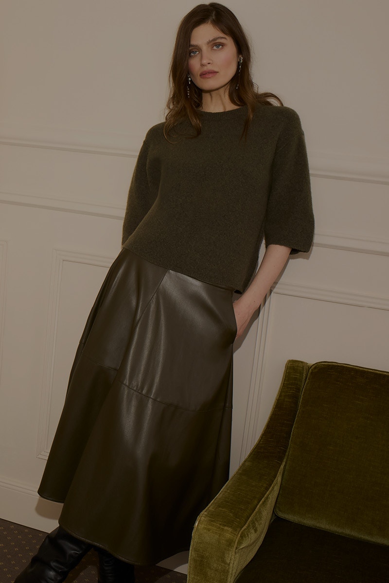 Woman with short-sleeved jumper in green and black skirt.