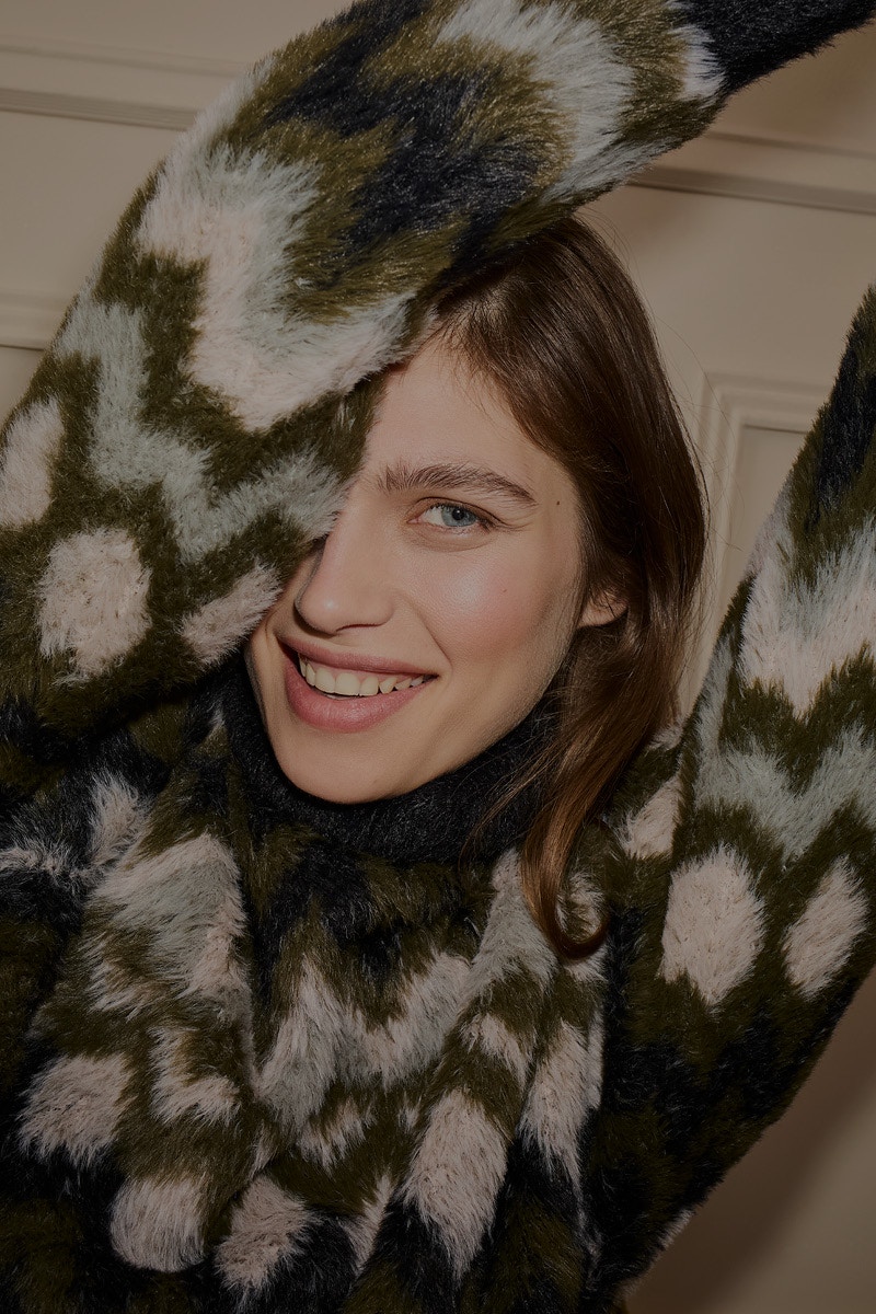 Close-up of a smiling woman wearing a patterned jumper in green, brown and white.