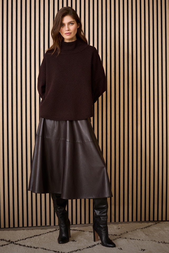 Woman with a brown jumper and a matching leather-look skirt in black.