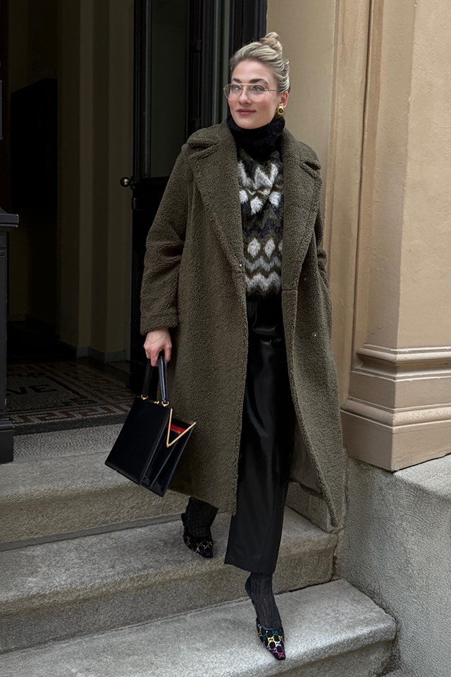 Influencerin Oleysa Schuler trägt unseren Mantel in khaki, darunter einen Rollkragen Strickpullover in schwarz, khaki, weiss und rose gemustert mit einer schwarzen Hose in Lederoptik.