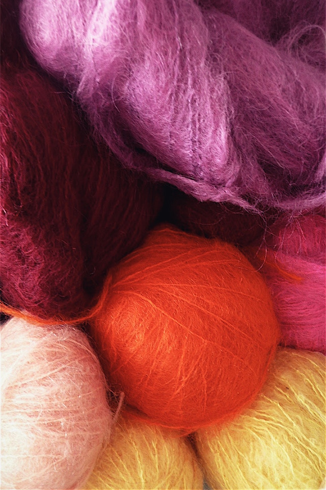 The image shows several balls of wool in white, yellow, orange, purple and pink.