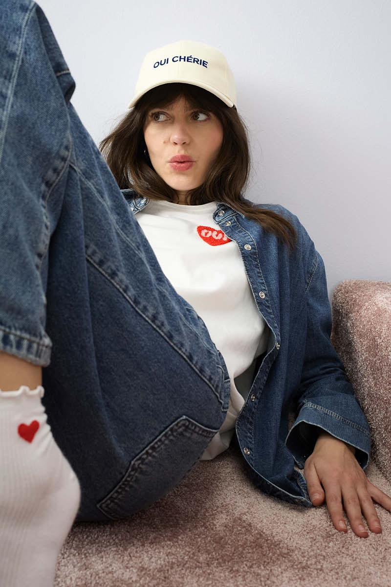 Eine Frau liegt am Boden, sie trägt eine offene Jeansbluse mit einem weissen Shirt mit einem roten Herz an der Brust und dazu eine passende Jeanshose.