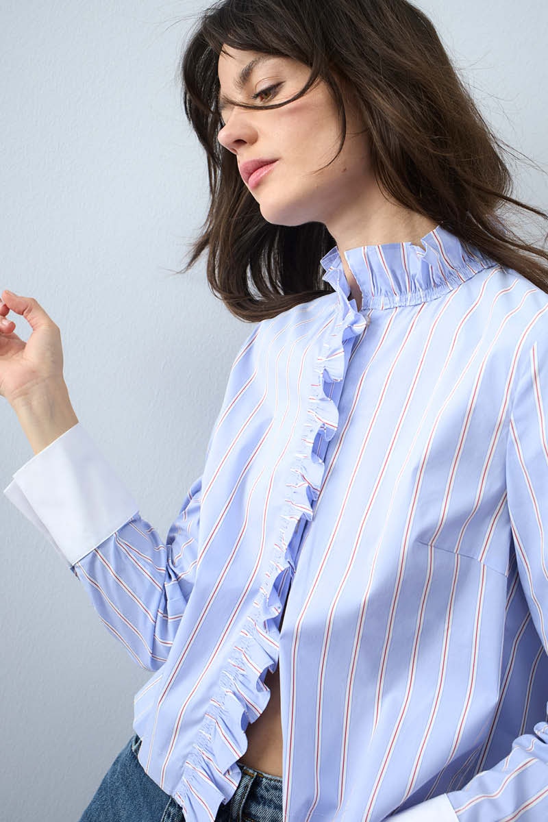 Woman wearing a light blue blouse with a striped pattern, ruffles on the collar and hem, and a white cuff.