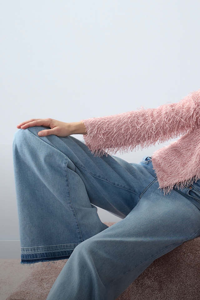 Woman wearing a printed T-shirt and a pink cardigan with fringes, paired with light blue jeans.