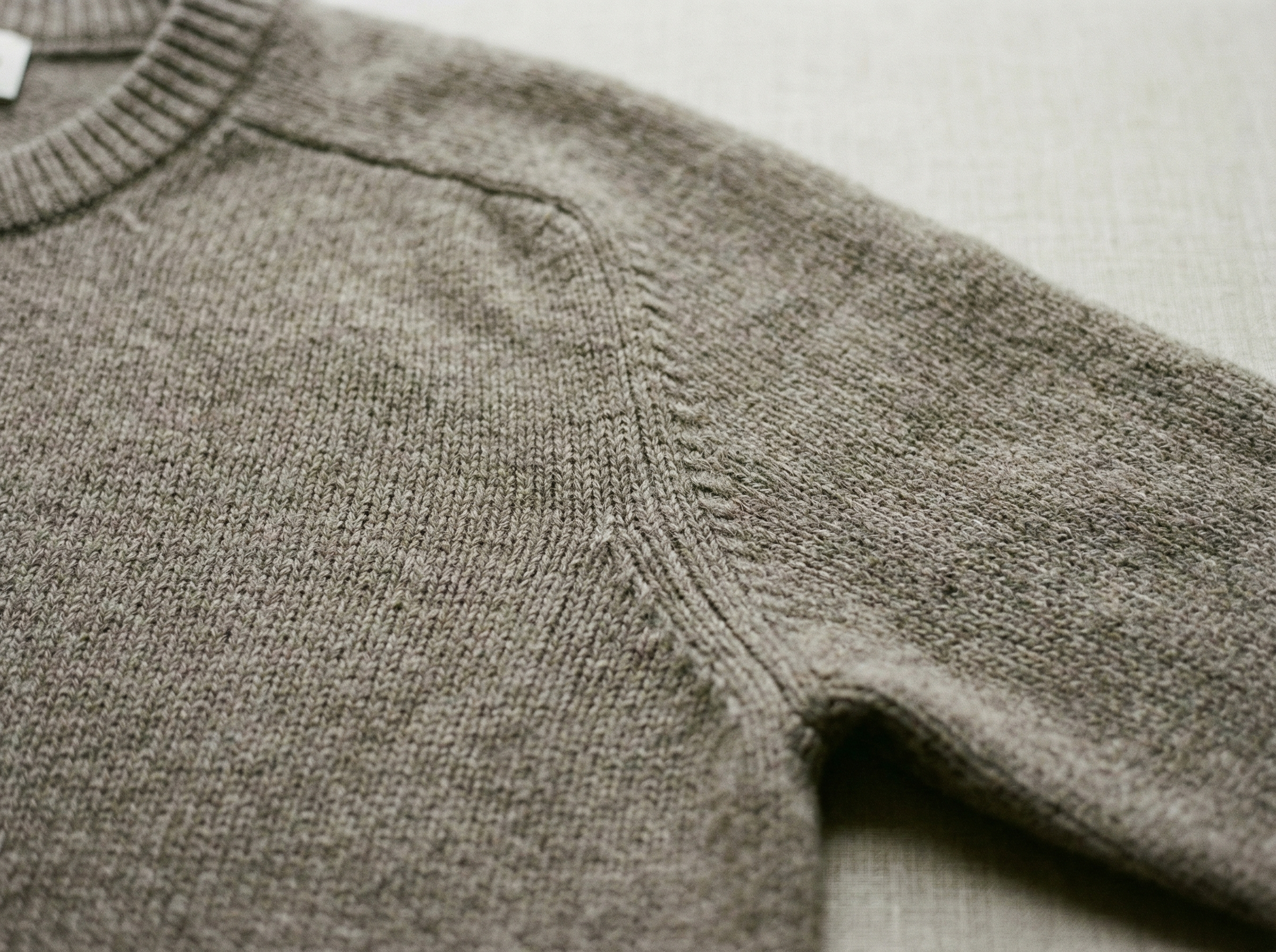 Ein gelegter grauner Pullover in einer Nahaufnahme der rechten Seite in fully fashion gestrickt.