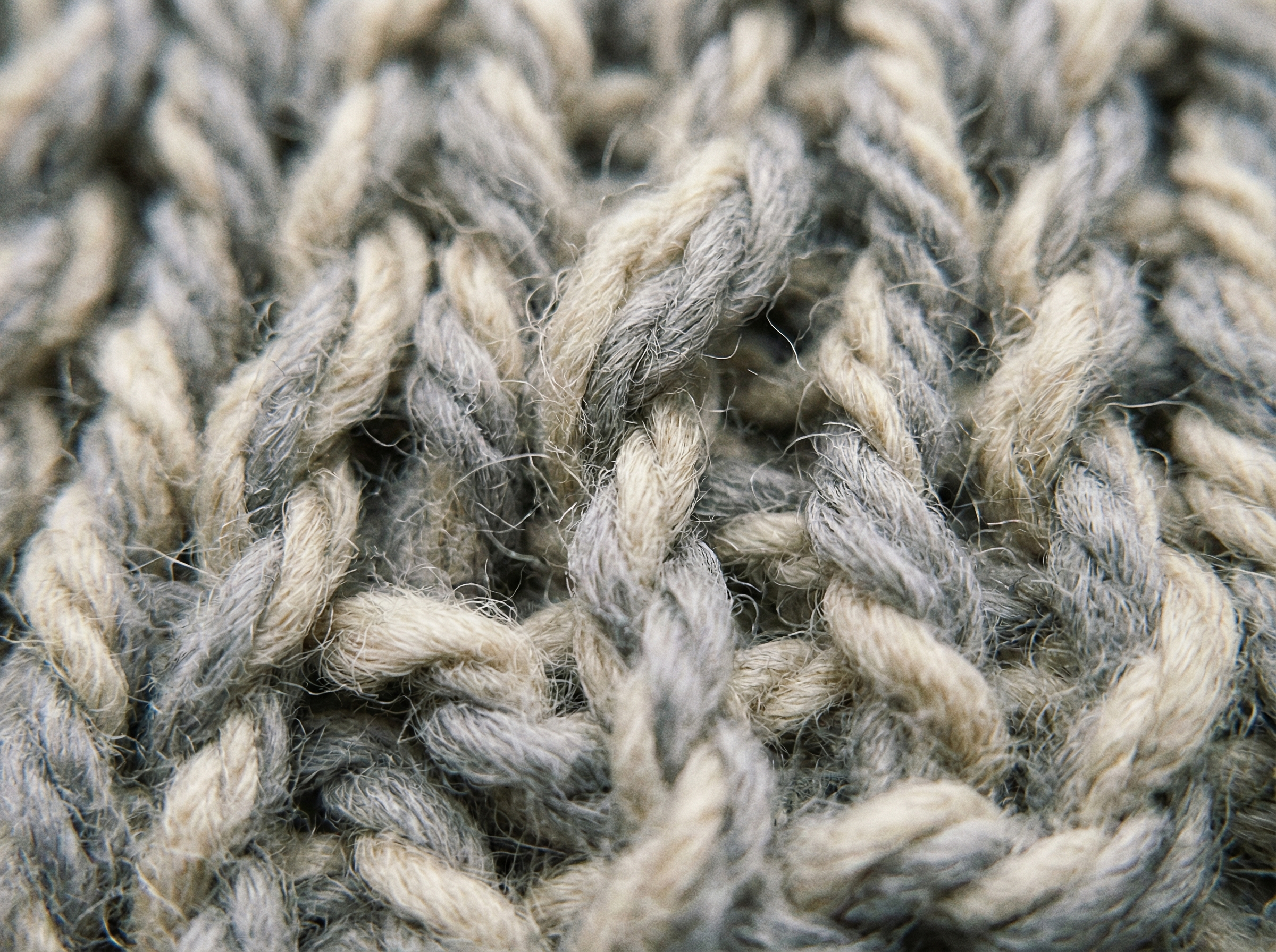 Extreme close-up of chunky grey and beige yarn showing twisted, textured knit stitches.