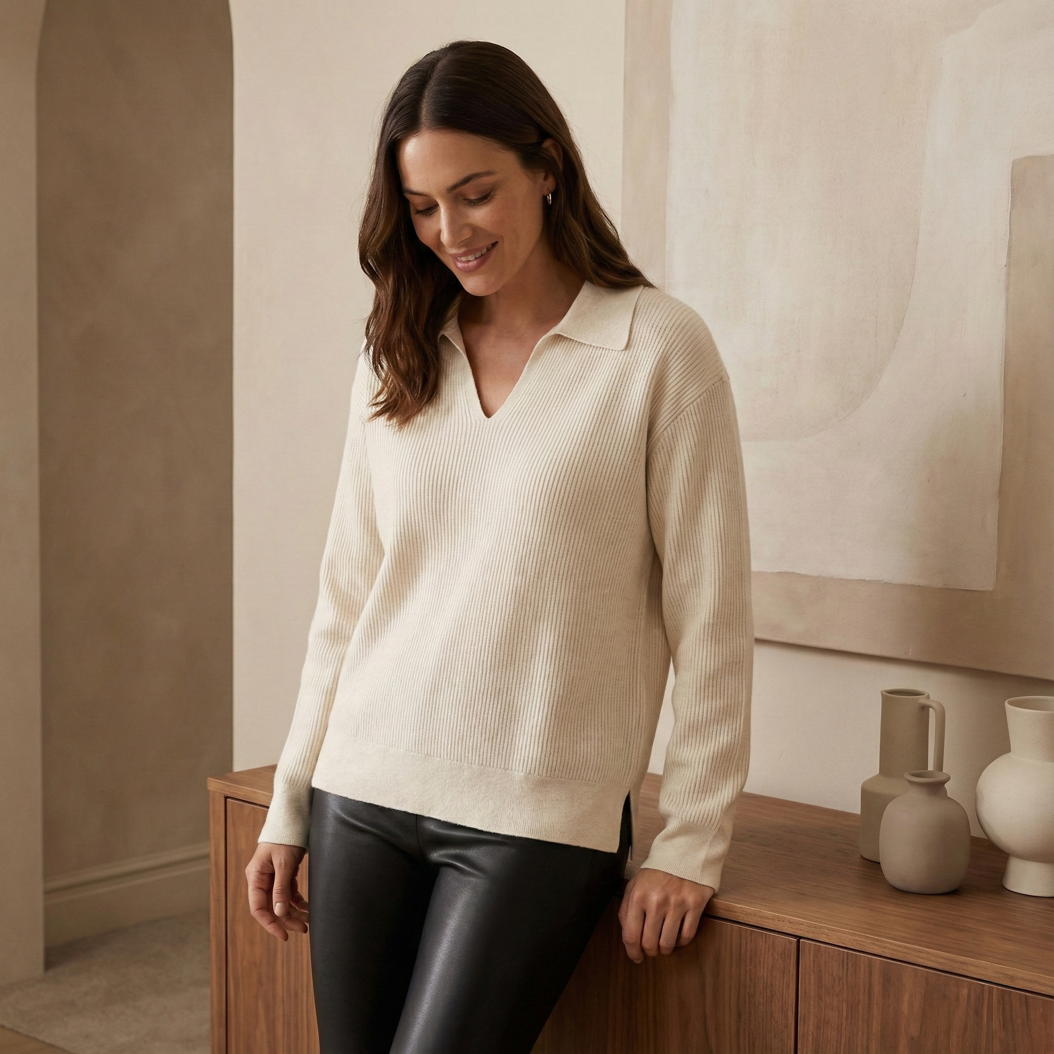 Eine Frau trägt einen cremefarbenen Strickpullover mit Polokragen und kombiniert ihn mit einer schwarzen Lederleggings