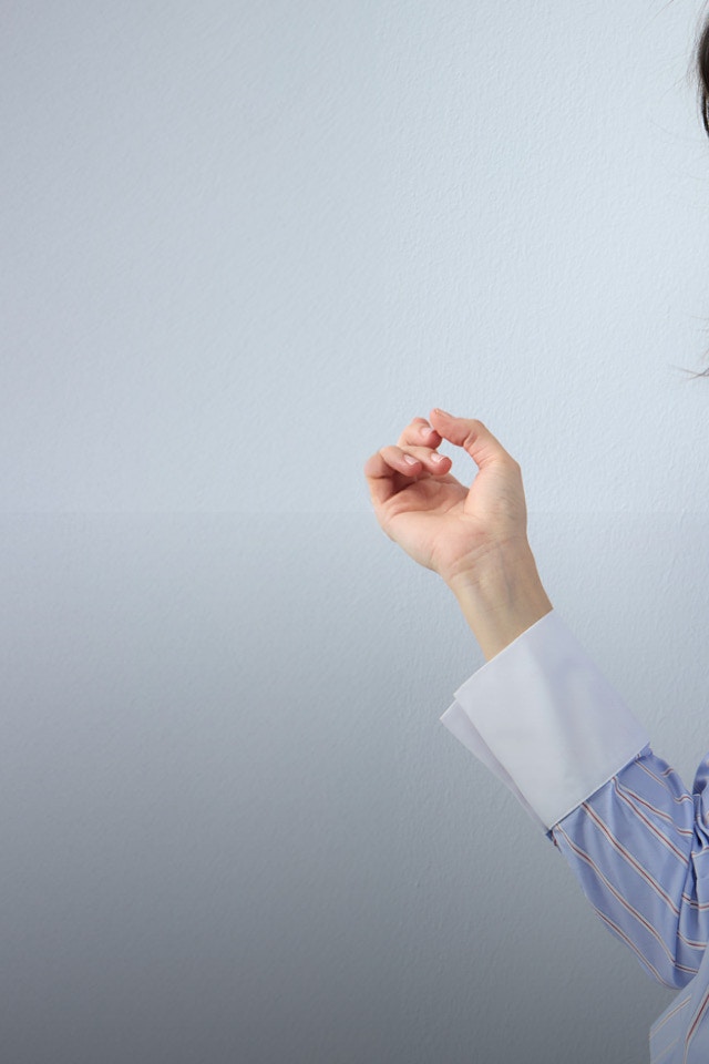 A woman wears a light blue striped blouse with ruffles on the collar and along the button placket, paired with jeans..