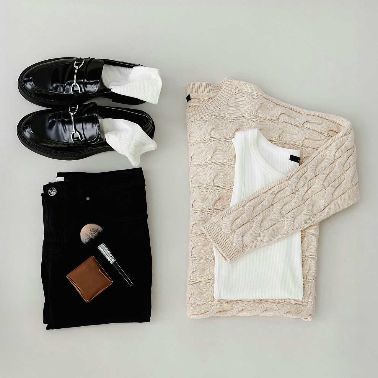 Flat, fashionable women's outfit with black loafers, white top, beige cardigan, black trousers and make-up accessories.