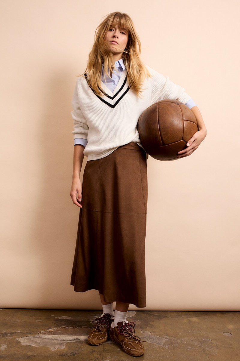 Frau mit beigem Pullover mit braunem V-Ausschnitt und braunem Rock.