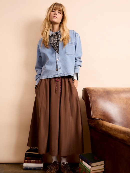 A woman is wearing a denim blouse with a brown skirt.