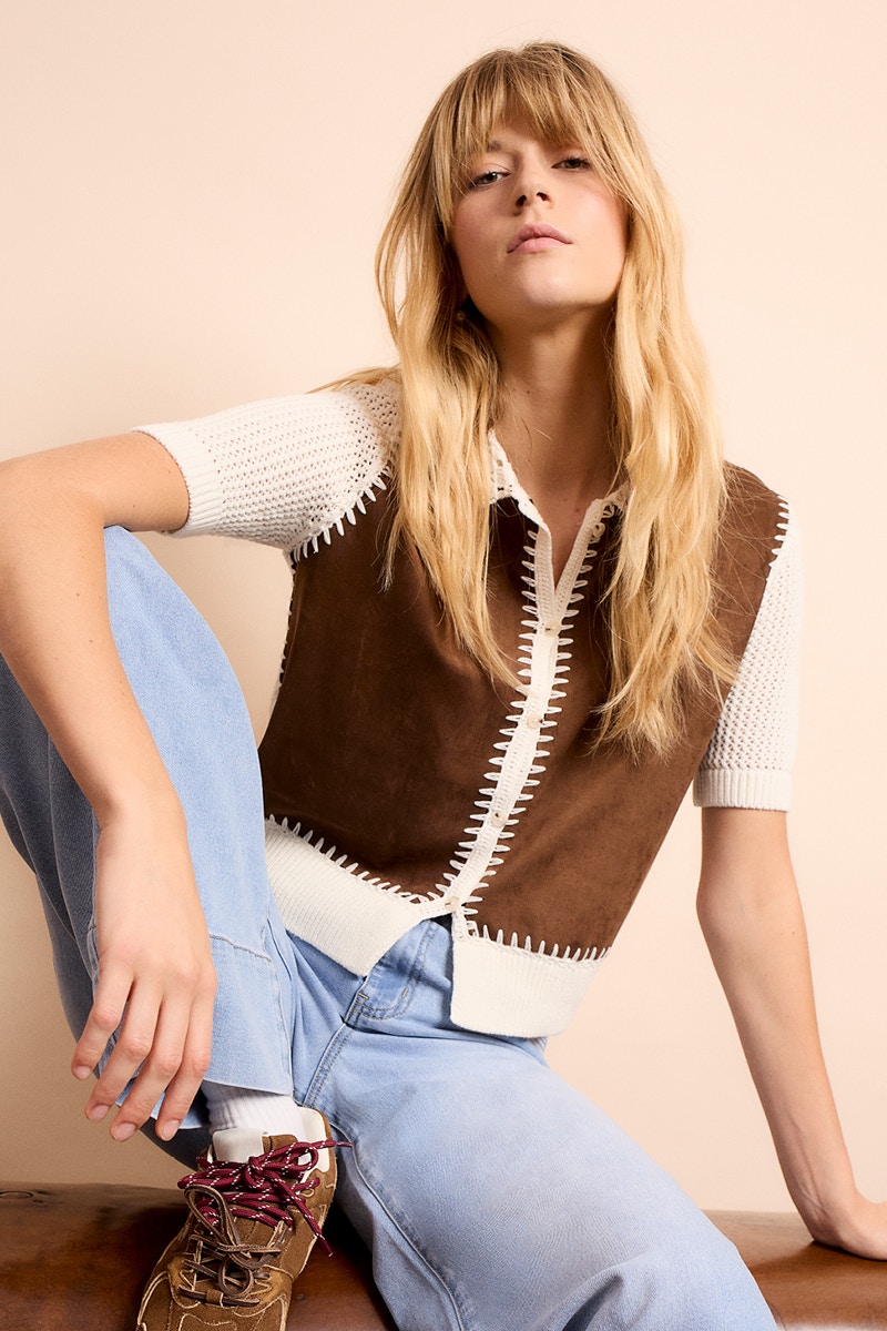 Woman wearing a white jumper with a contrasting brown bodysuit and jeans.