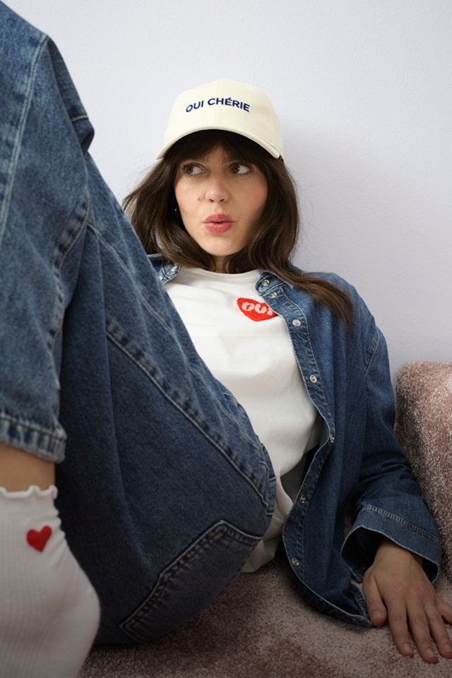 Eine Frau liegt am Boden, sie trägt eine offene Jeansbluse mit einem weissen Shirt mit einem roten Herz an der Brust und dazu eine passende Jeanshose.