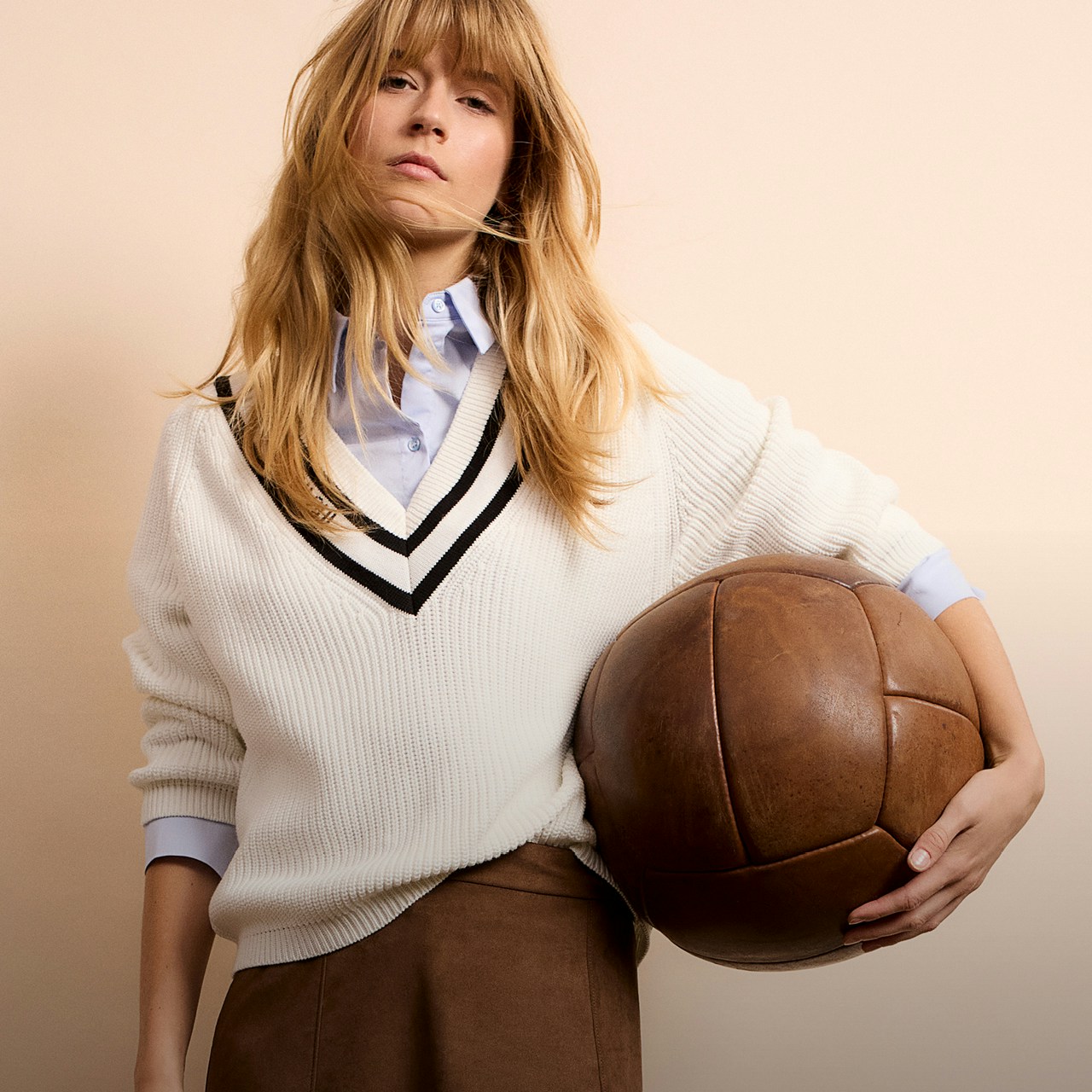 Frau mit beigem Pullover mit braunem V-Ausschnitt und braunem Rock.