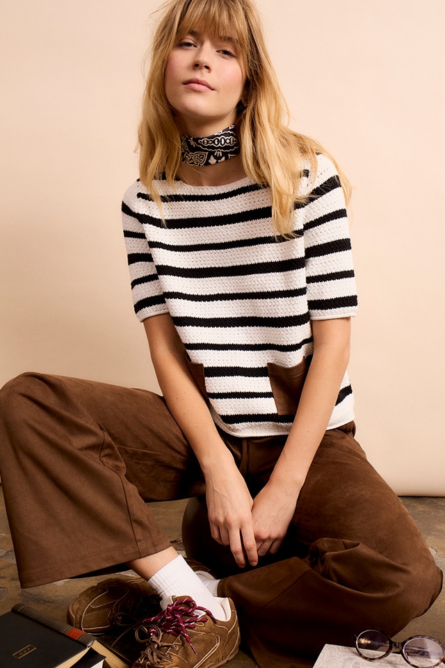 Woman wearing a striped short-sleeved jumper in white and brown with a brown patch pocket at stomach level, paired with brown trousers.