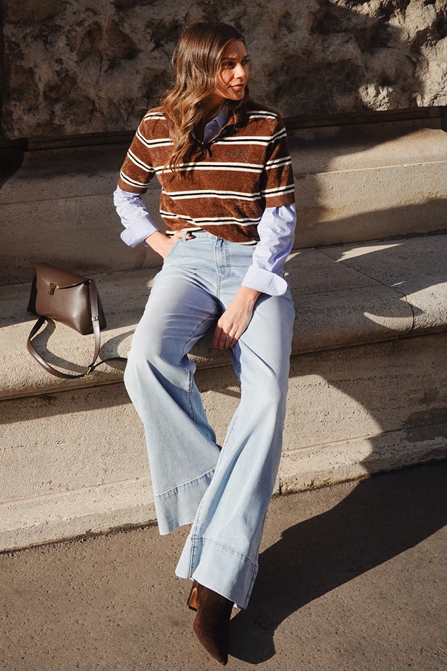 Influencerin Raffaela Wachter trägt unser braun weiss gestreiftes Poloshirt, eine blaue gestreifte Bluse darunter und kompletiert den Look mit ner hellen Jeans.