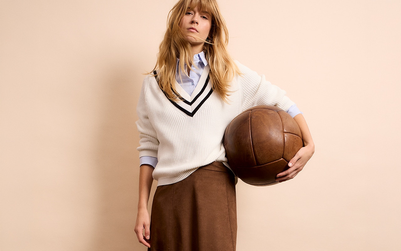 Woman wearing a beige jumper with a brown V-neck and a brown skirt.