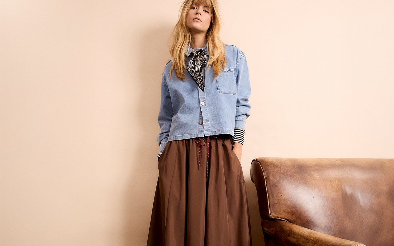 A woman is wearing a denim blouse and a brown skirt.