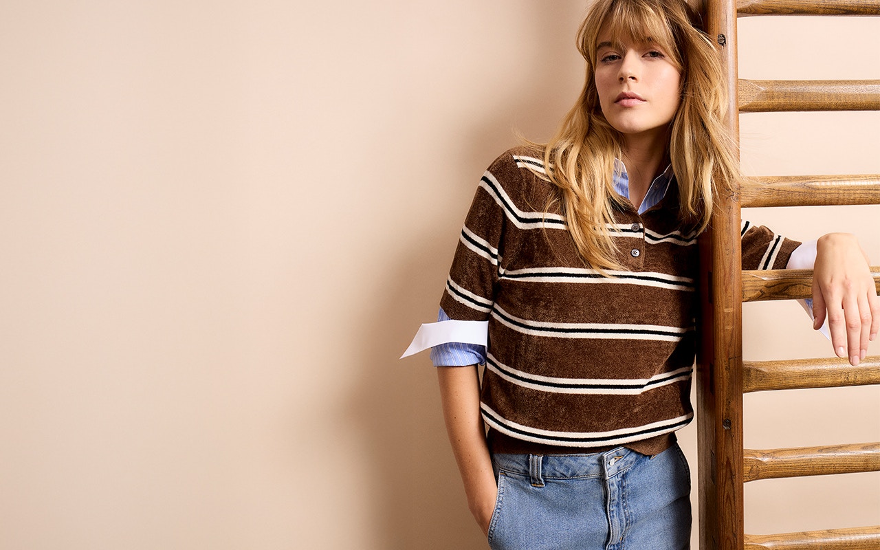 Woman wearing a brown and white shirt with a blouse underneath and a denim skirt.
