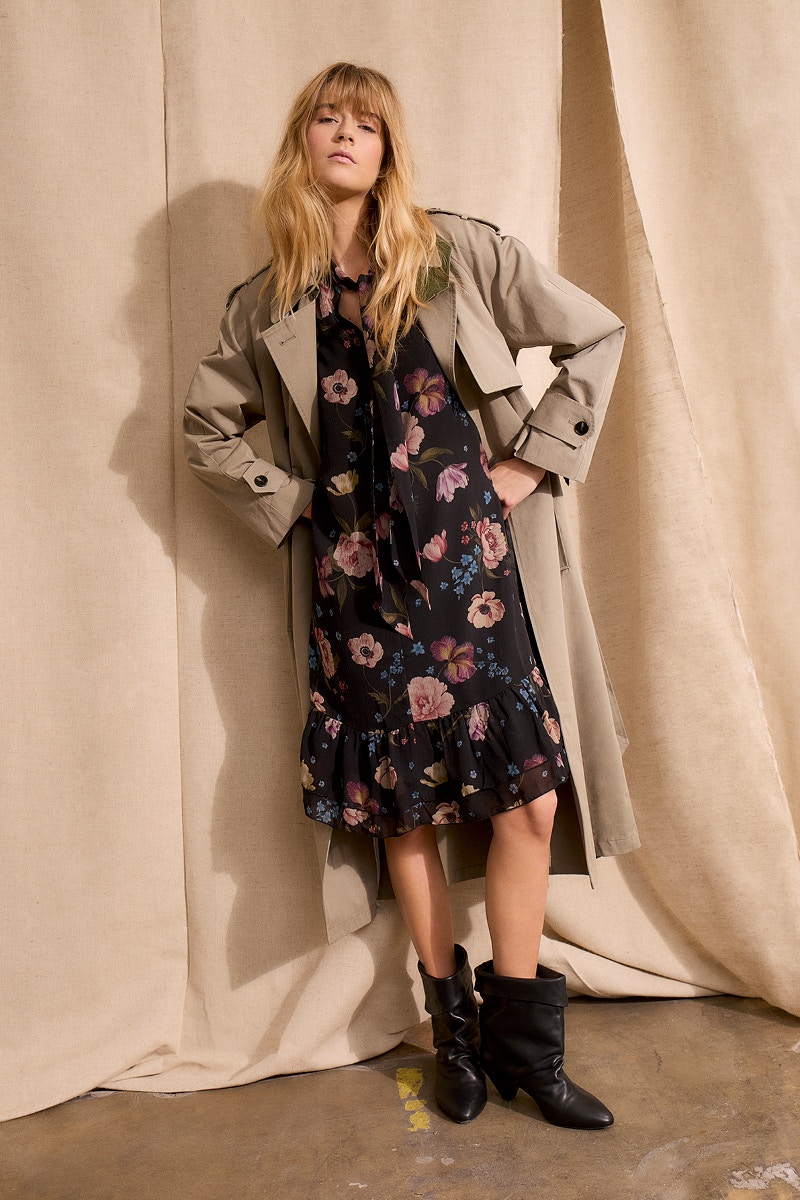 Model trägt ein schwarzes Kleid mit floralem Print in Rosa, Grün, Gelb und Blau, kombiniert mit einem hellen Trenchcoat. Feminine Damenmode aus den Oui Kollektionen auf oui.com.