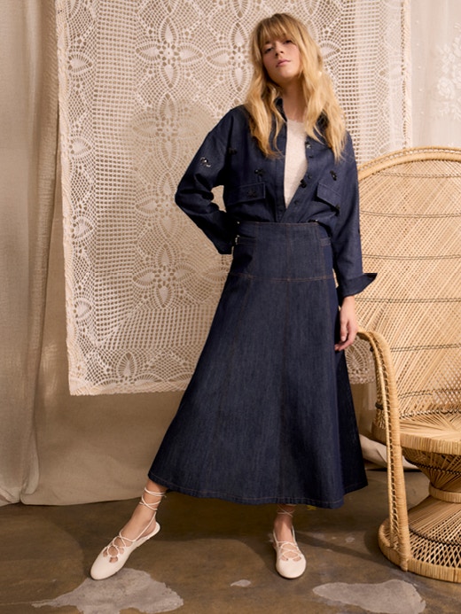 The woman is wearing a dark blue denim blouse with a matching midi skirt and a white jumper underneath the denim blouse.