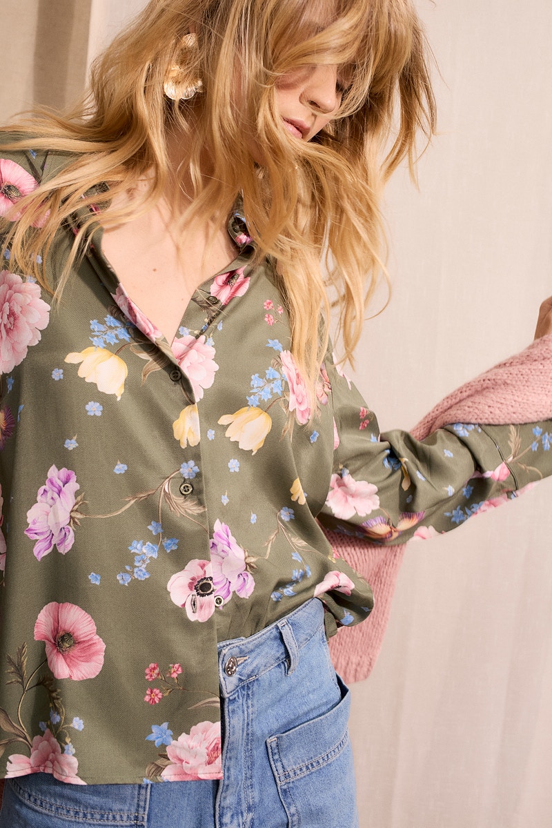 Model wears an olive green blouse with a floral print in pink, yellow and blue, paired with light blue jeans. Feminine women's fashion from the Oui collections at oui.com.