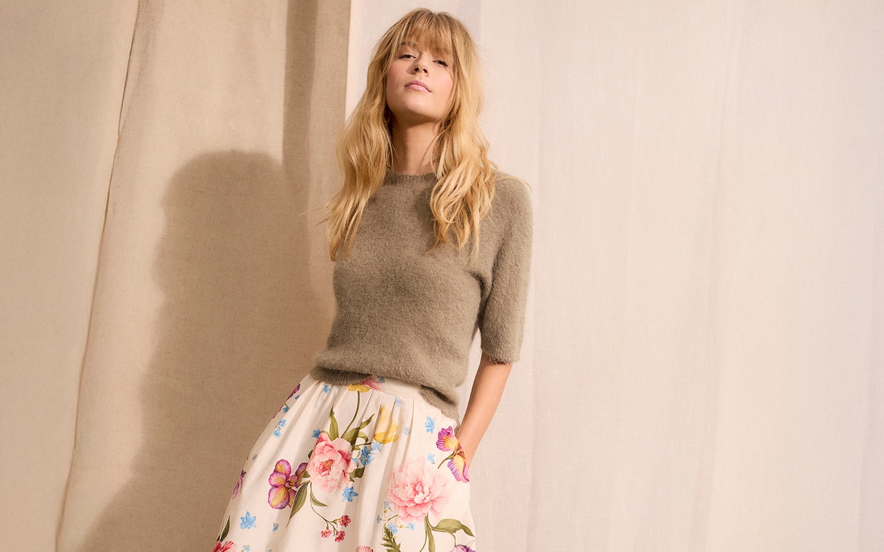 Woman wearing a green jumper with a white skirt with a colourful floral pattern.
