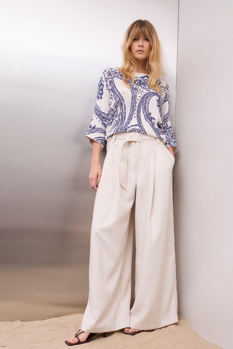 Frau trägt einen weißen Pullover mit einem blauen Paisleymuster und einer beigen Hose.