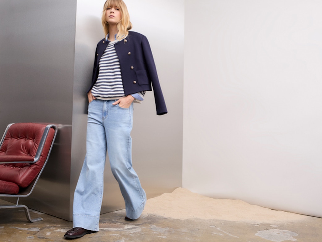 Frau trägt einen blau weiss gestreiften Pullover, eine blaue Jacke darüber und eine Jeans.