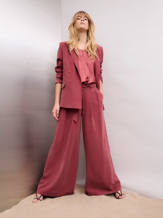 Woman wearing a raspberry red suit consisting of a blazer and wide-leg trousers, paired with a pink slip-on blouse.