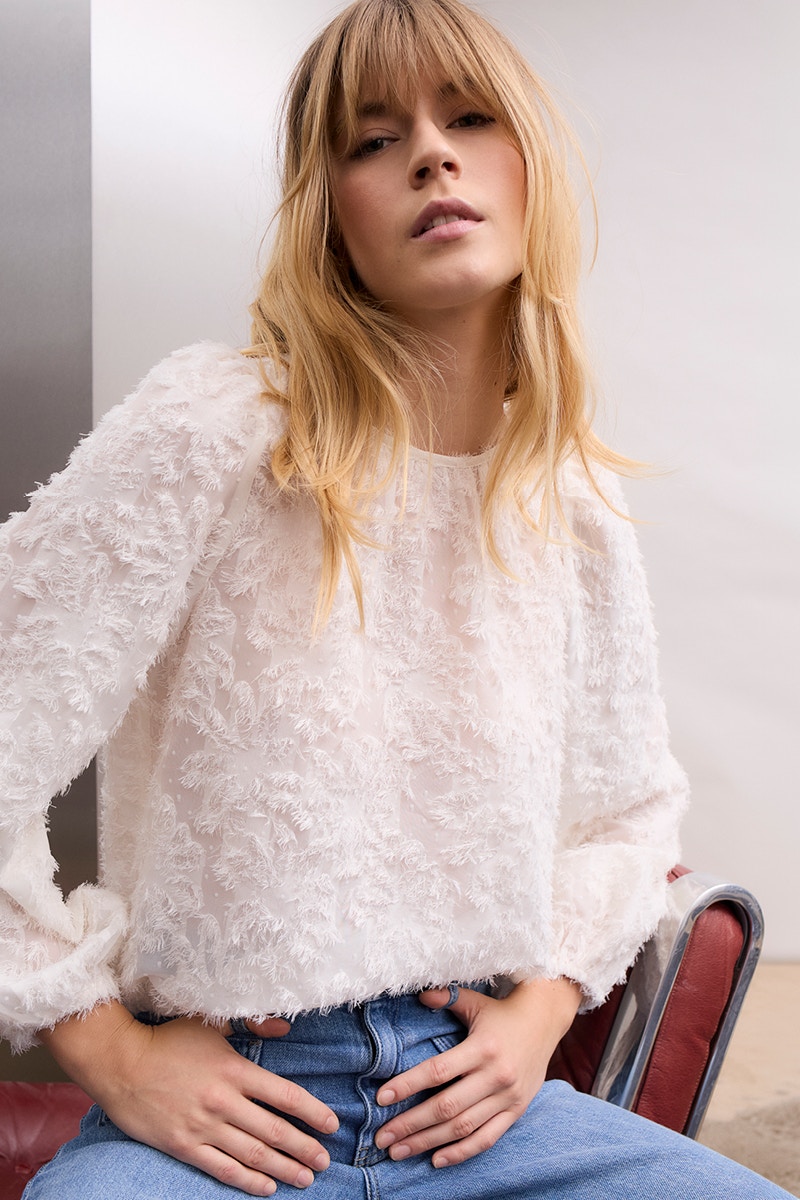 Woman wearing a white blouse with a floral pattern and jeans.