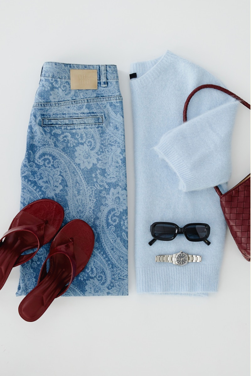 Clothes laid out: on the left, a pair of paisley jeans; on the right, a light blue knitted jumper.