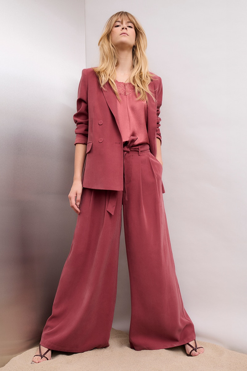 Woman wearing a raspberry red suit consisting of a blazer and wide-leg trousers, paired with a pink slip-on blouse.