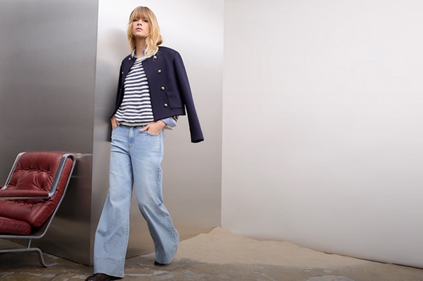 Woman wearing a dark blue jacket, underneath a blue and white striped knitted jumper and jeans.