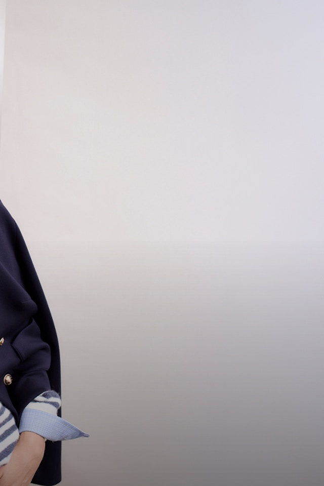 Frau trägt eine dunkelblaue Jacke, darunter ein blau-weiss gestreiften Strickpullover.