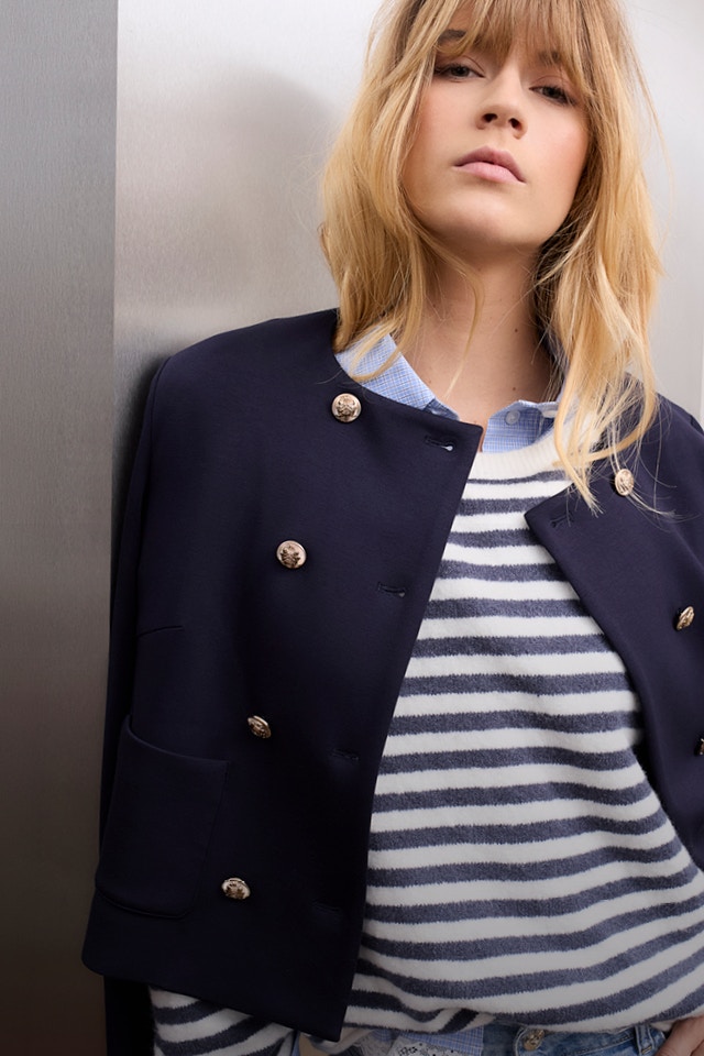 Woman wearing a dark blue jacket, underneath a blue and white striped knitted jumper.